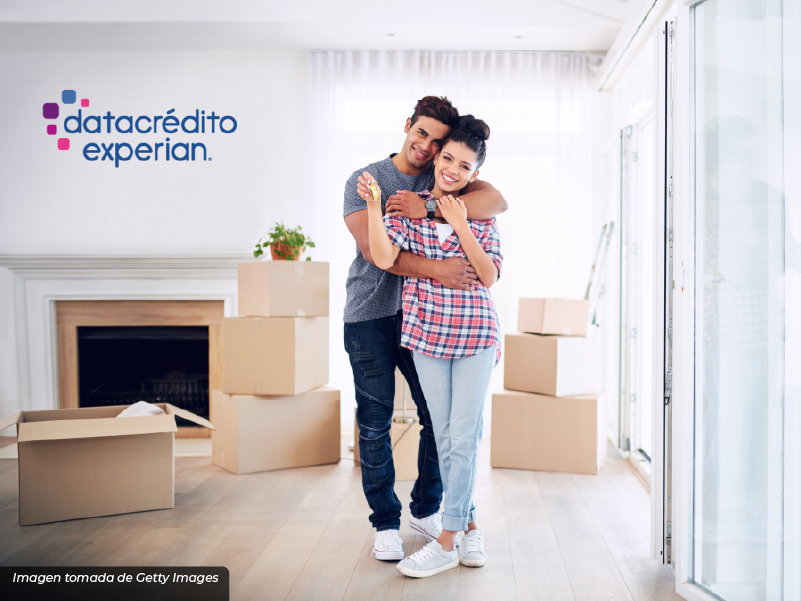 Imagen de una pareja de novios abrazandose en una casa nueva con cajas abiertas en la parte de atrás.