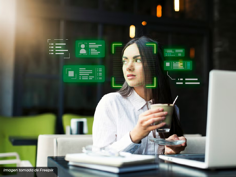 Mujer sentada en una cafetería, sosteniendo una taza mientras observa hologramas verdes digitales relacionados con inteligencia artificial y análisis de datos.